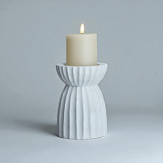 White carved hurricane lantern with candle, creating ambient lighting and patterned shadows for decoration.